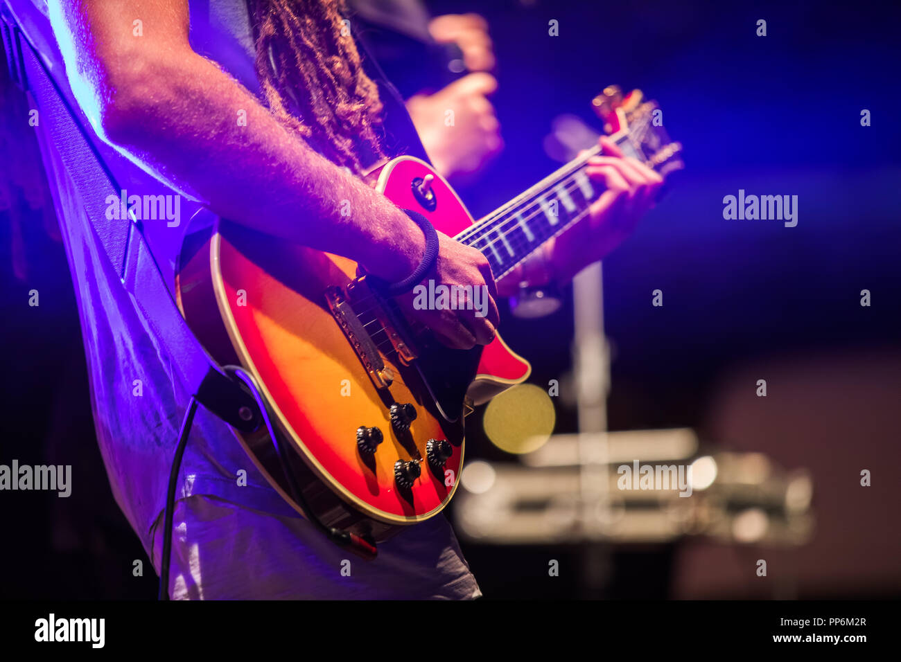 Guitarist playing on electric bass guitar on stage. Colorful, soft