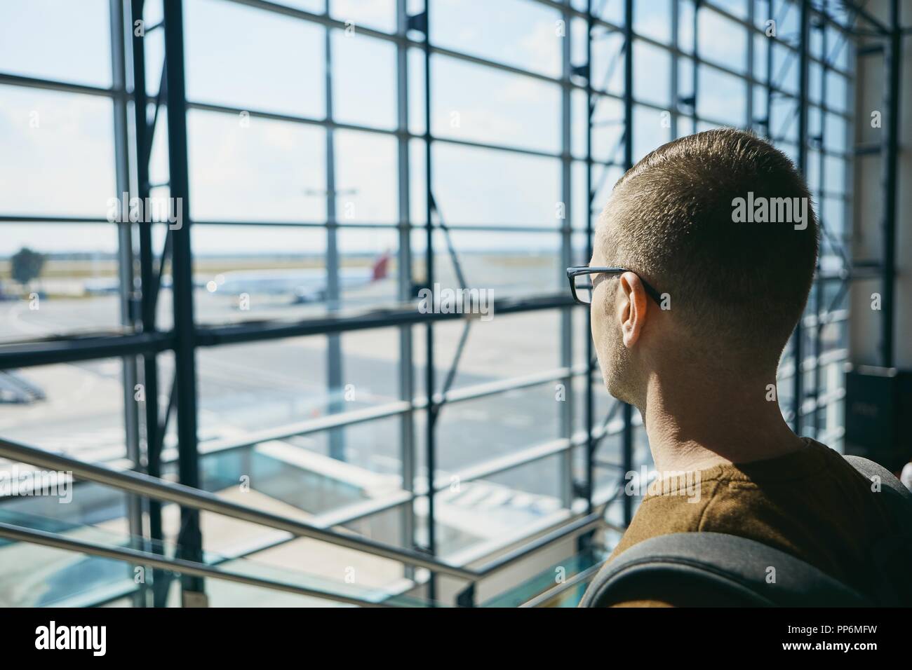 Young passenger waiting at airport and looking through window to airplane. Stock Photo