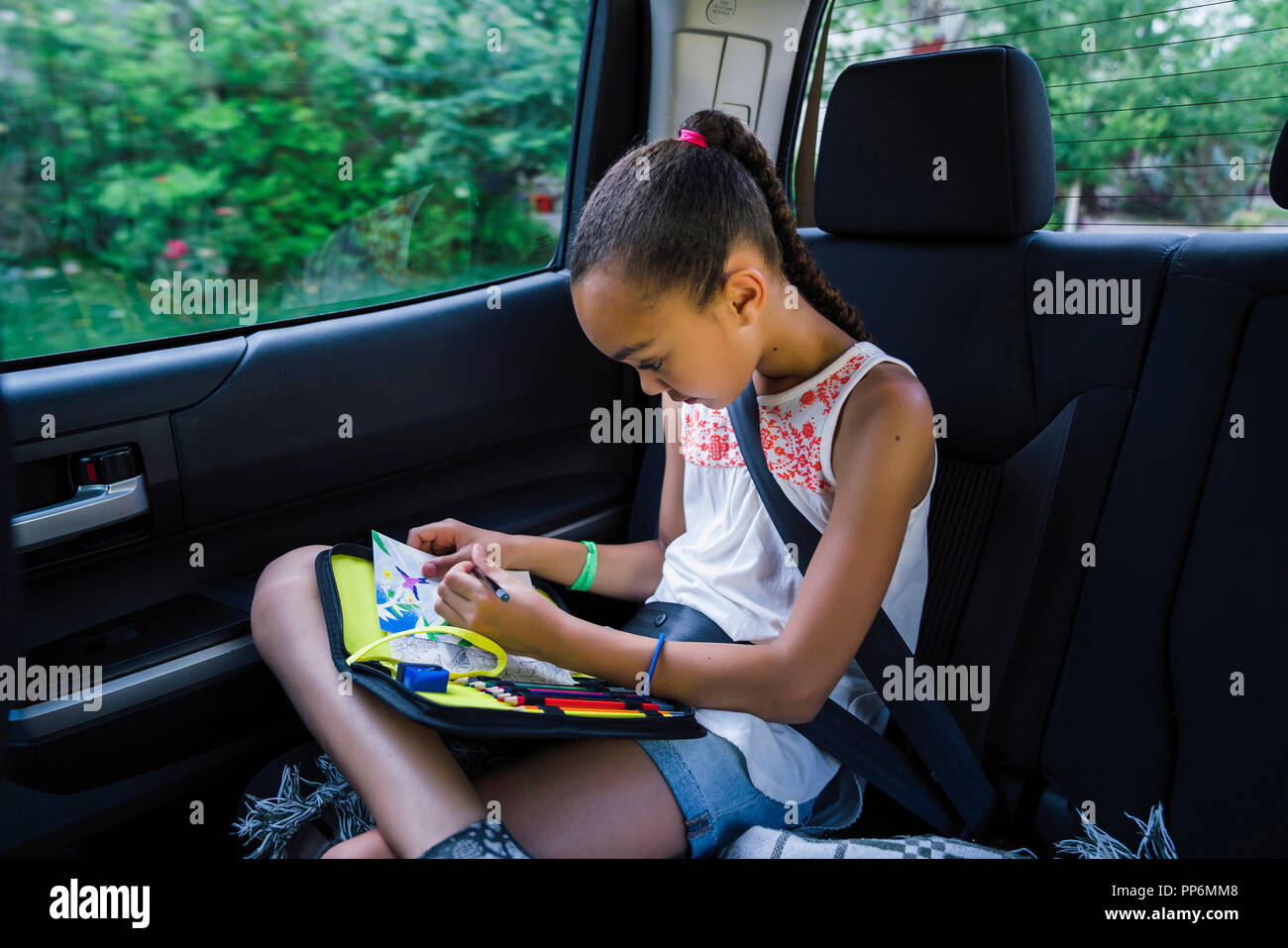 Girl drawing with colored pencils in back seat of car Stock Photo