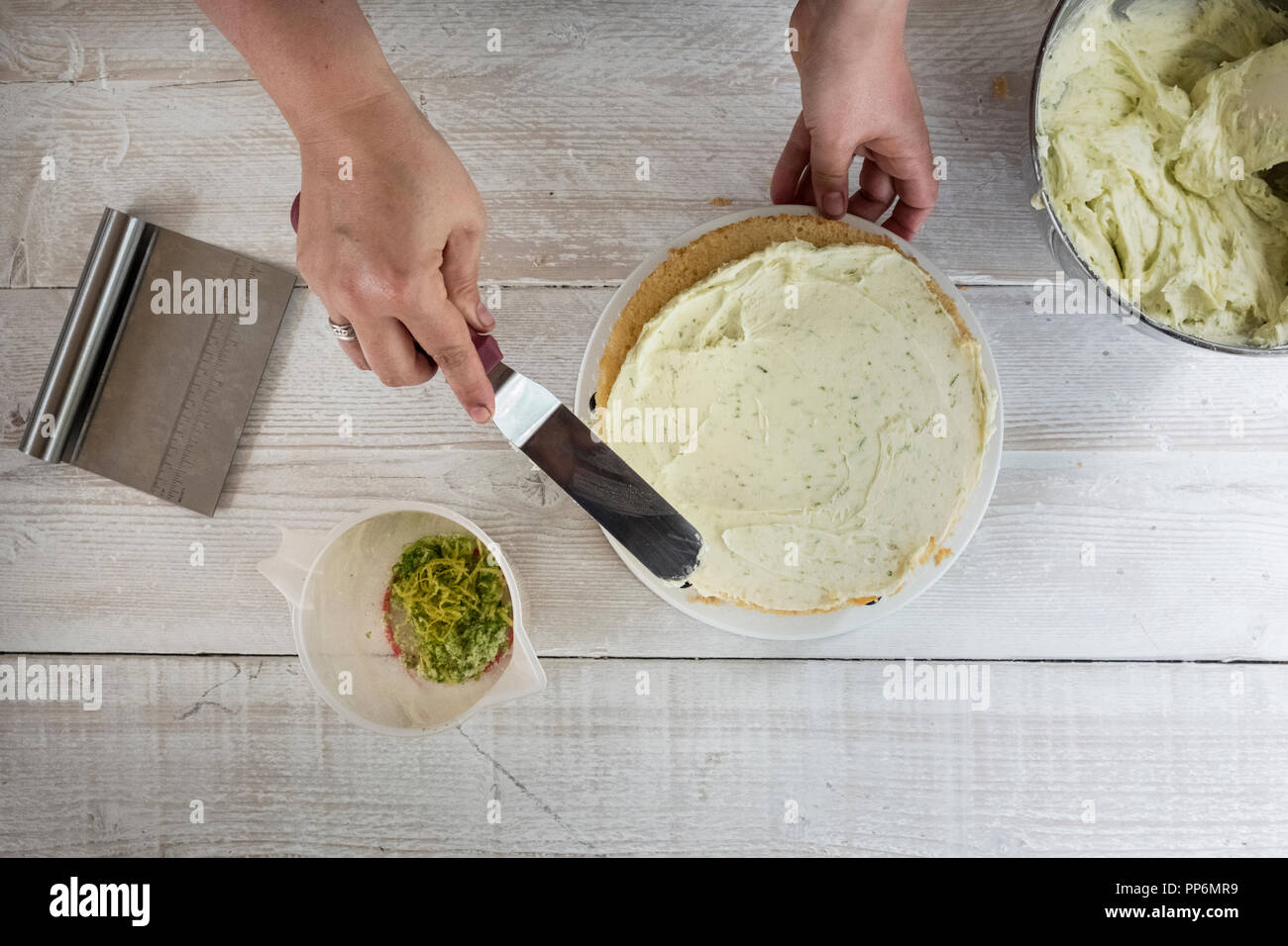 High angle view of a person smoothing buttercream icing over a fresh baked gin and tonic flavoured cake. Stock Photo