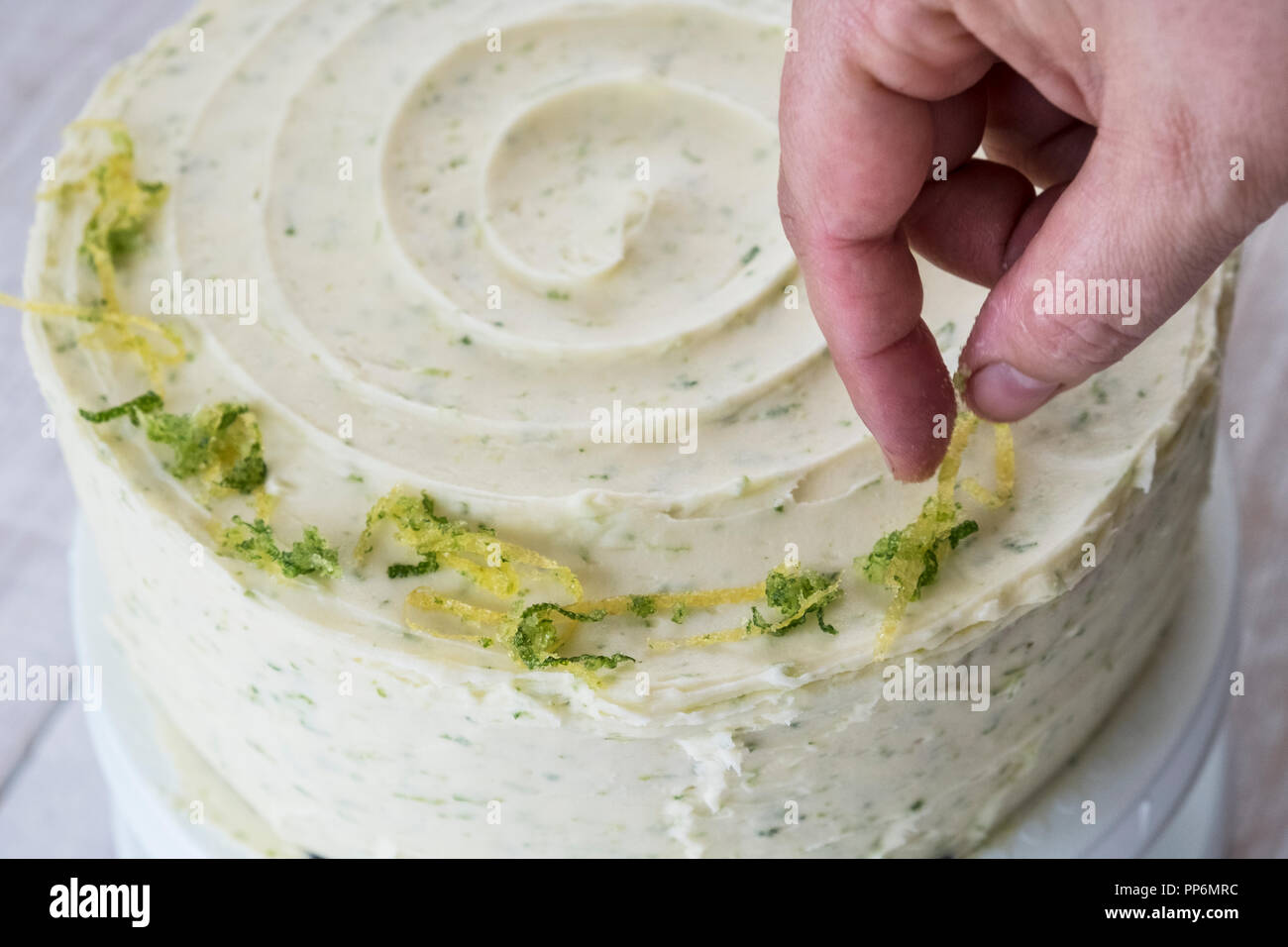 High angle view of a person decorating a gin and tonic cake white icing and with green grated lime zest. Stock Photo