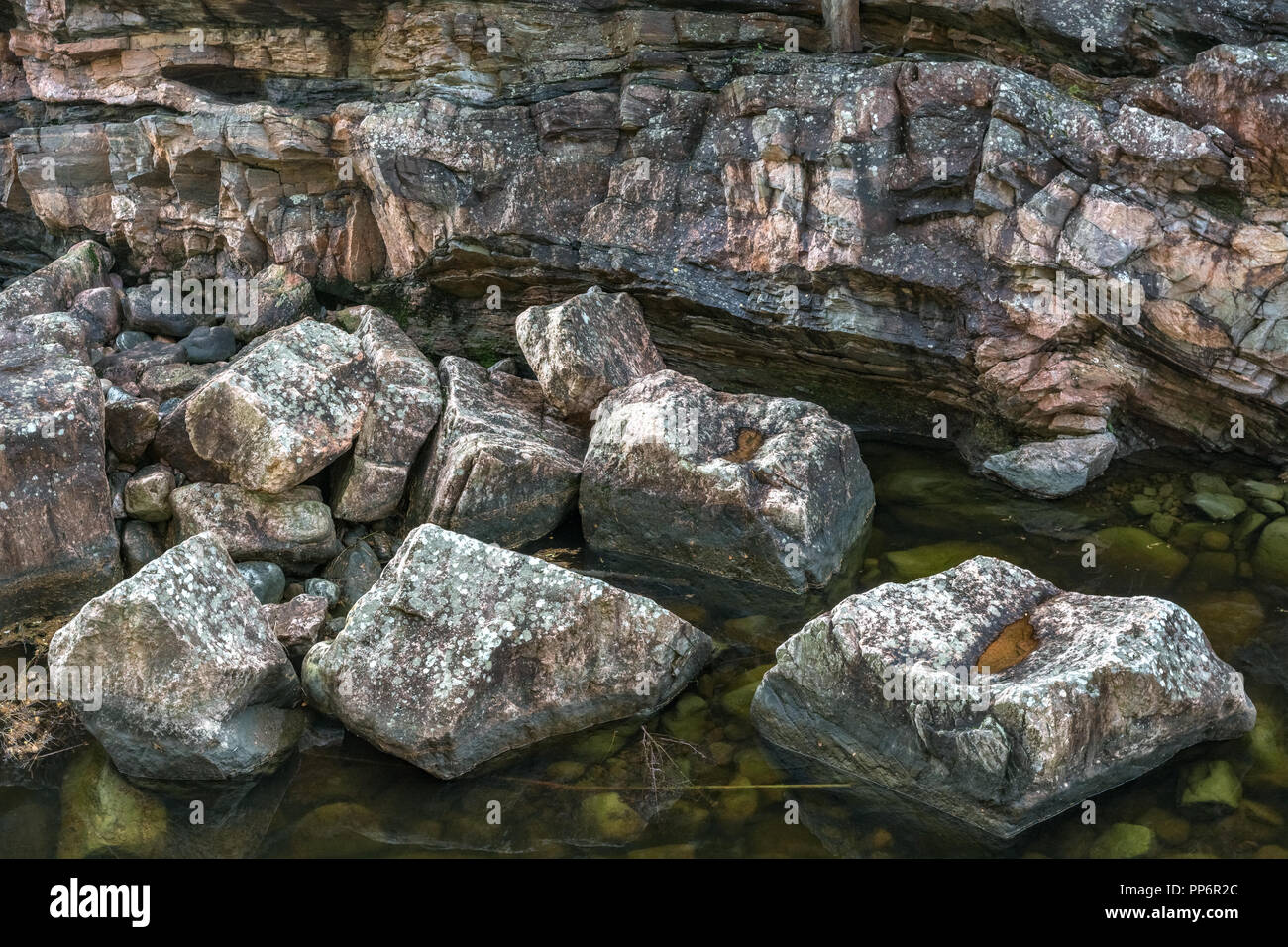 A steep rocky shore with a stone of pink shade and large boulders on the bottom of the half-dried riverbed. Stock Photo