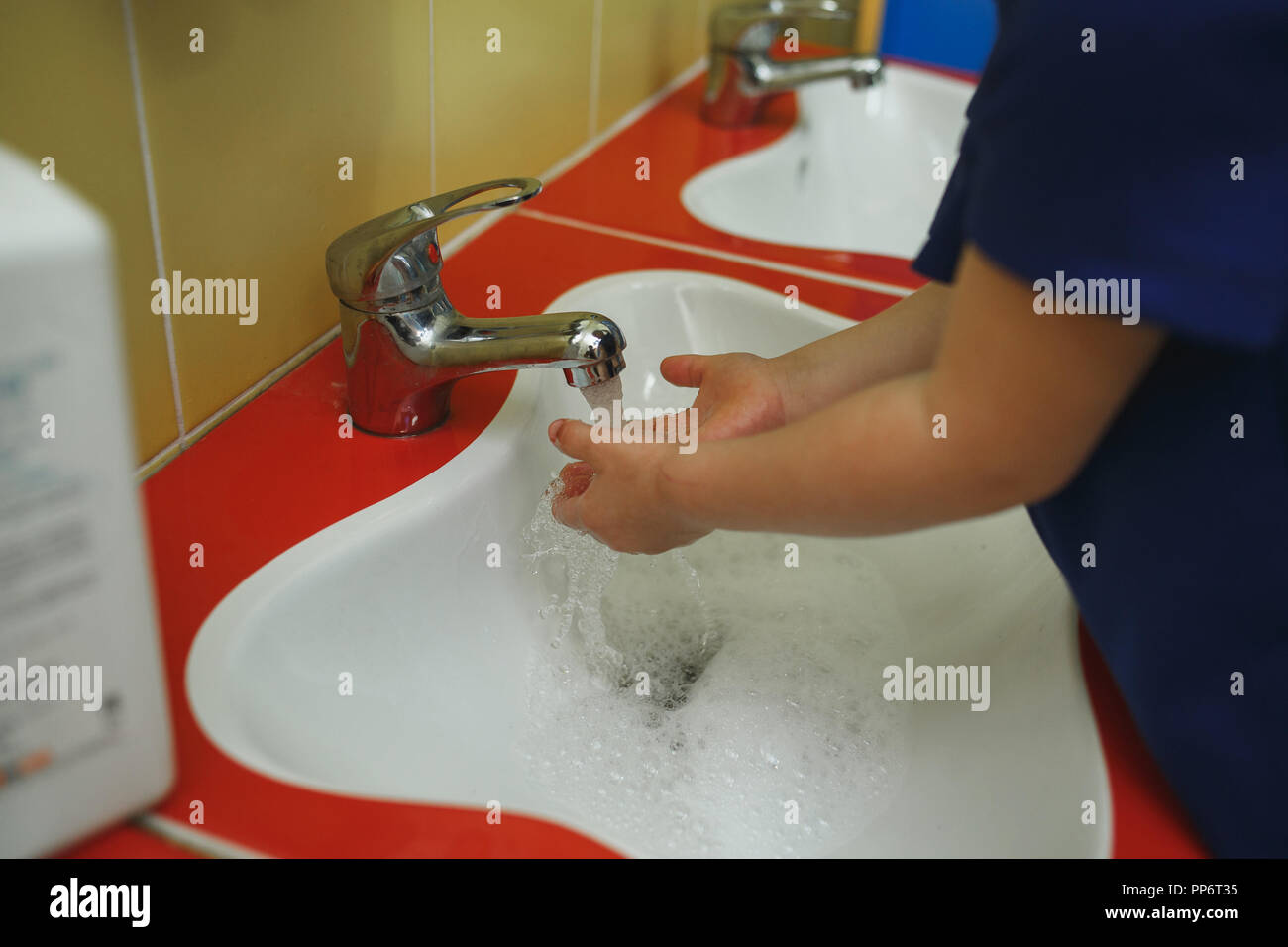 Child washing hands with soap in bathroom in kindergarten. Stock Photo