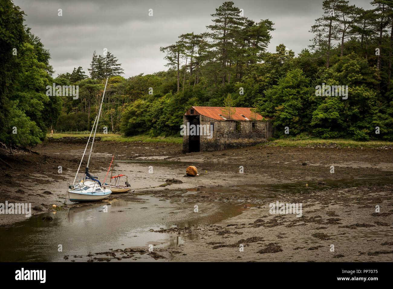 Two boats lie in a muddy river bed not too far from an apparently abandoned building. Stock Photo
