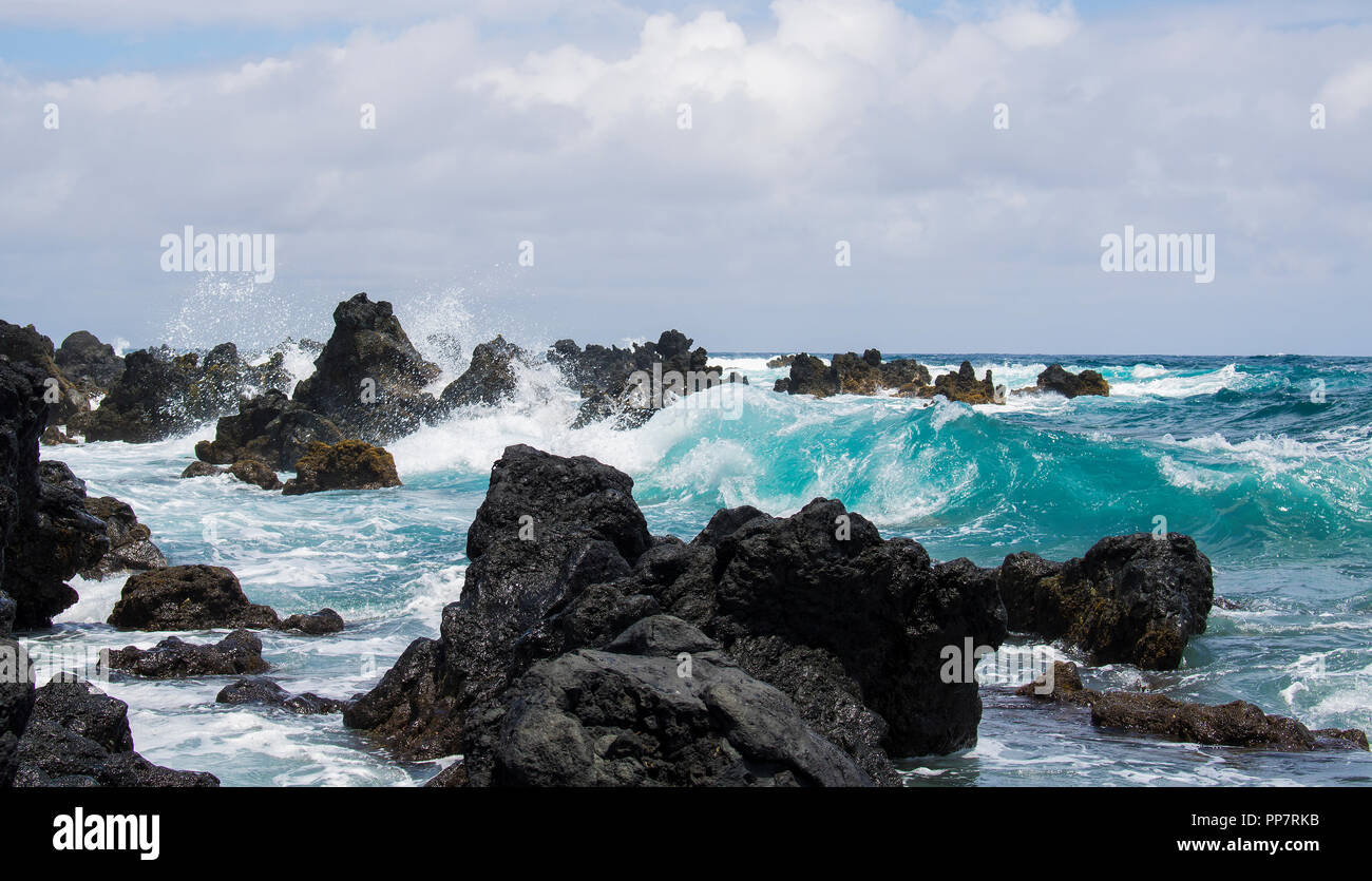 Rough Lava Coastline with Turquoise Colored Wave Curling and Breaking  Through Rocks Stock Photo