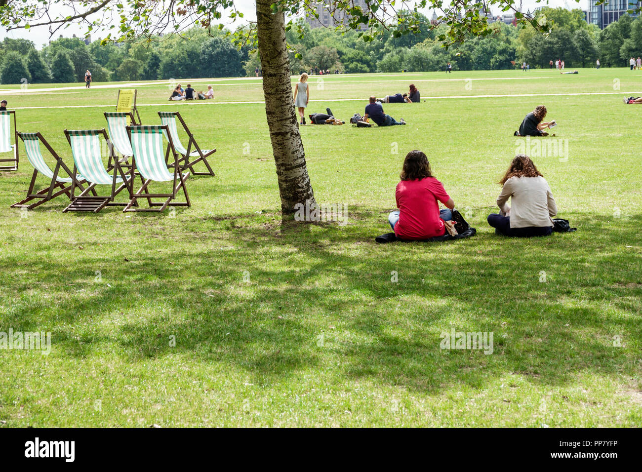 London England,UK,Hyde Park,historic Royal Park,field lawn,parade ground,rental deck chairs,shade tree,woman female women,sitting on grassy grass,UK G Stock Photo
