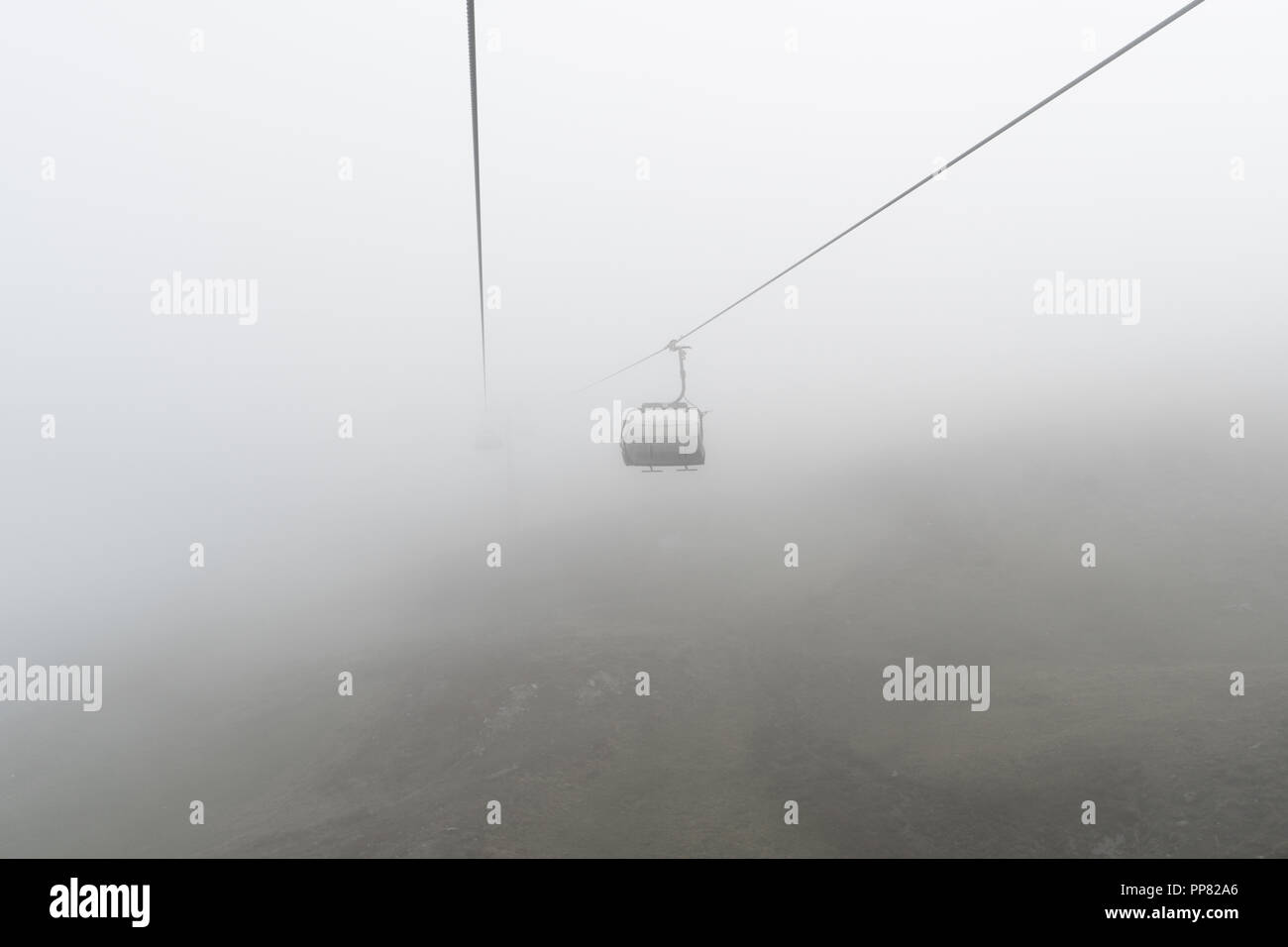 empty chairlift and cable in a bleak and foggy mountain landscape in the early autumn in a ski resort in Switzerland Stock Photo