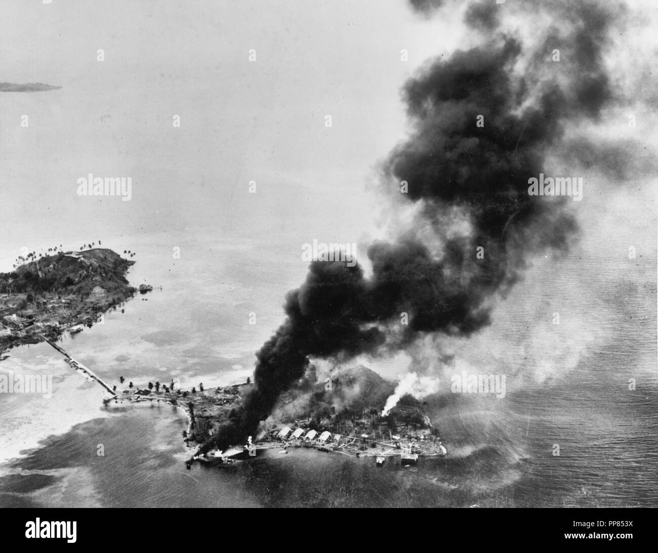 Guadalcanal-Tulagi Landings, 7-9 August 1942 - Fires burning among Japanese facilities and seaplanes on Tanambogo Island, east of Tulagi, on the invasion's first day, 7 August 1942. This view looks about SSW, with Gavutu Island to the left, connected to Tanambogo by a causeway. Stock Photo