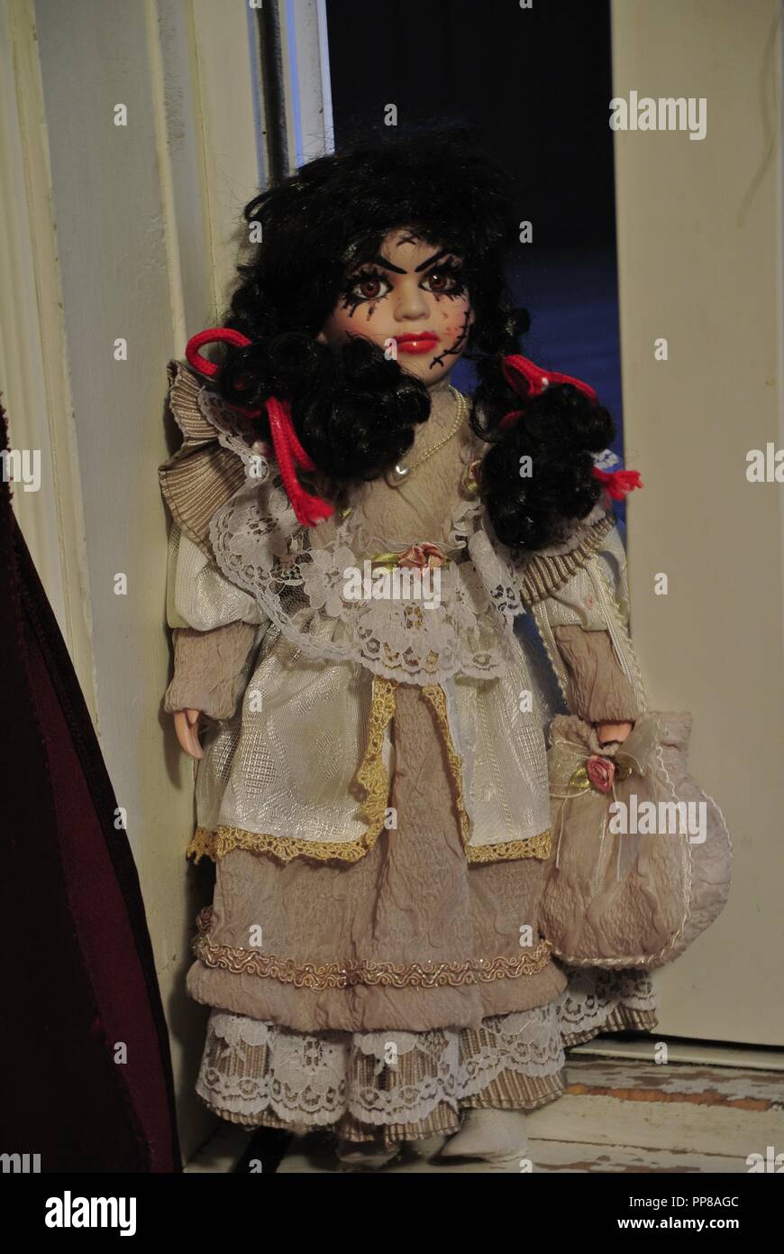 A creepy antique porcelain doll with long black hair and a scary, beautiful face with scars,,dressed in a white vintage dress, coming at you Halloween Stock Photo