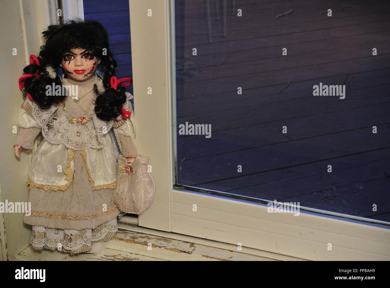 A creepy antique porcelain doll with long black hair and a scary, beautiful face with scars,,dressed in a white vintage dress, coming at you Halloween Stock Photo