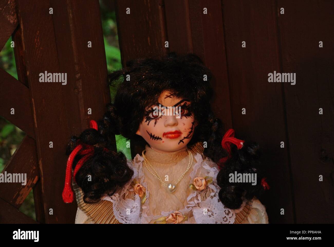 A close up of an antique porcelain doll with long black hair and a scary, beautiful face with scars;, dressed in a white vintage dress, Halloween Stock Photo