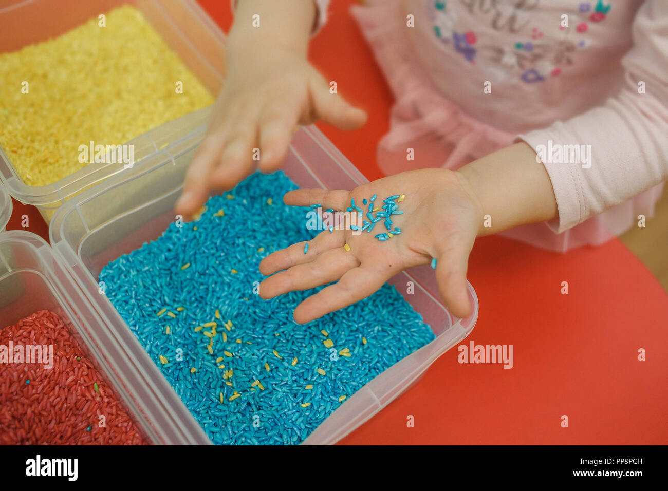 Toddler hands playing with rainbow rice in the sensory box. Baby's ...