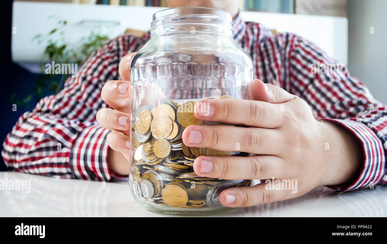 Closeup photo of young man holding glass jar full of coins Stock Photo