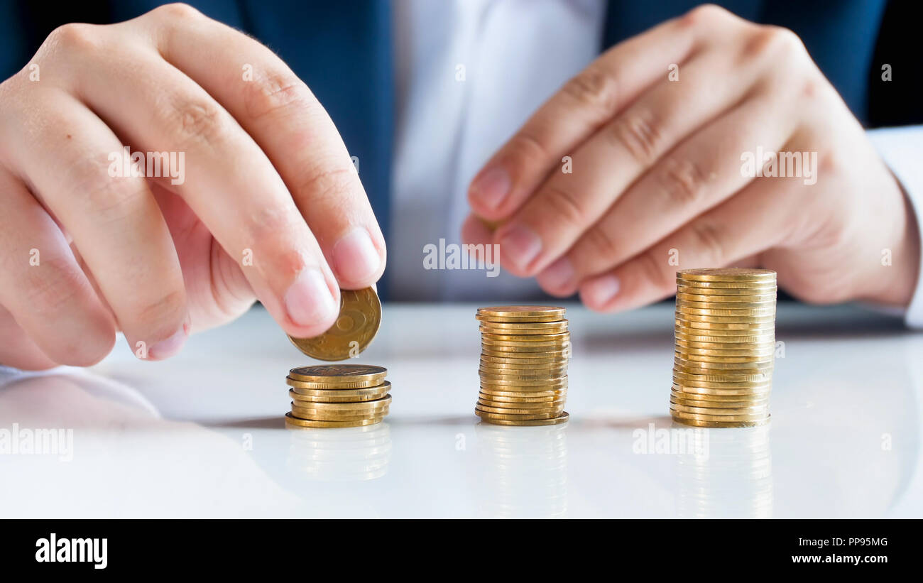 Closeup image of businessman sitting behind desk and putting coins in ...