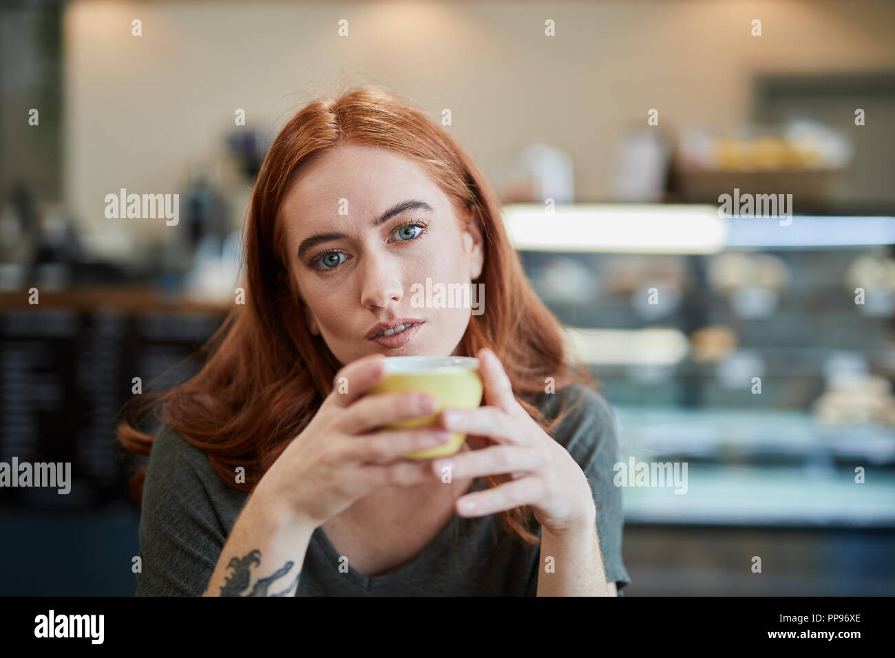A single female, sits in a city cafe holding a hot beverage in a cup