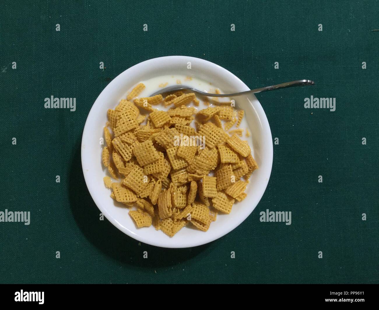 Bowel of square cereal in milk with spoon on green background. Stock Photo