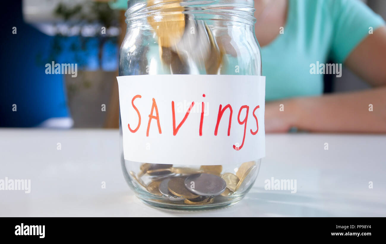 Closeup image of coins falling in glass jar labeled Savings Stock Photo