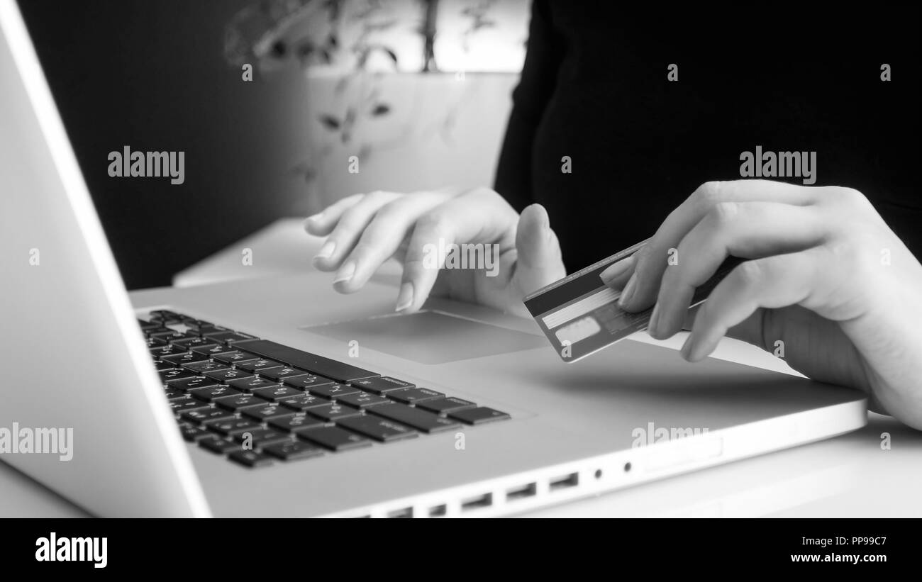 Black and white image of young woman typing on laptop and holding credit card in hand Stock Photo