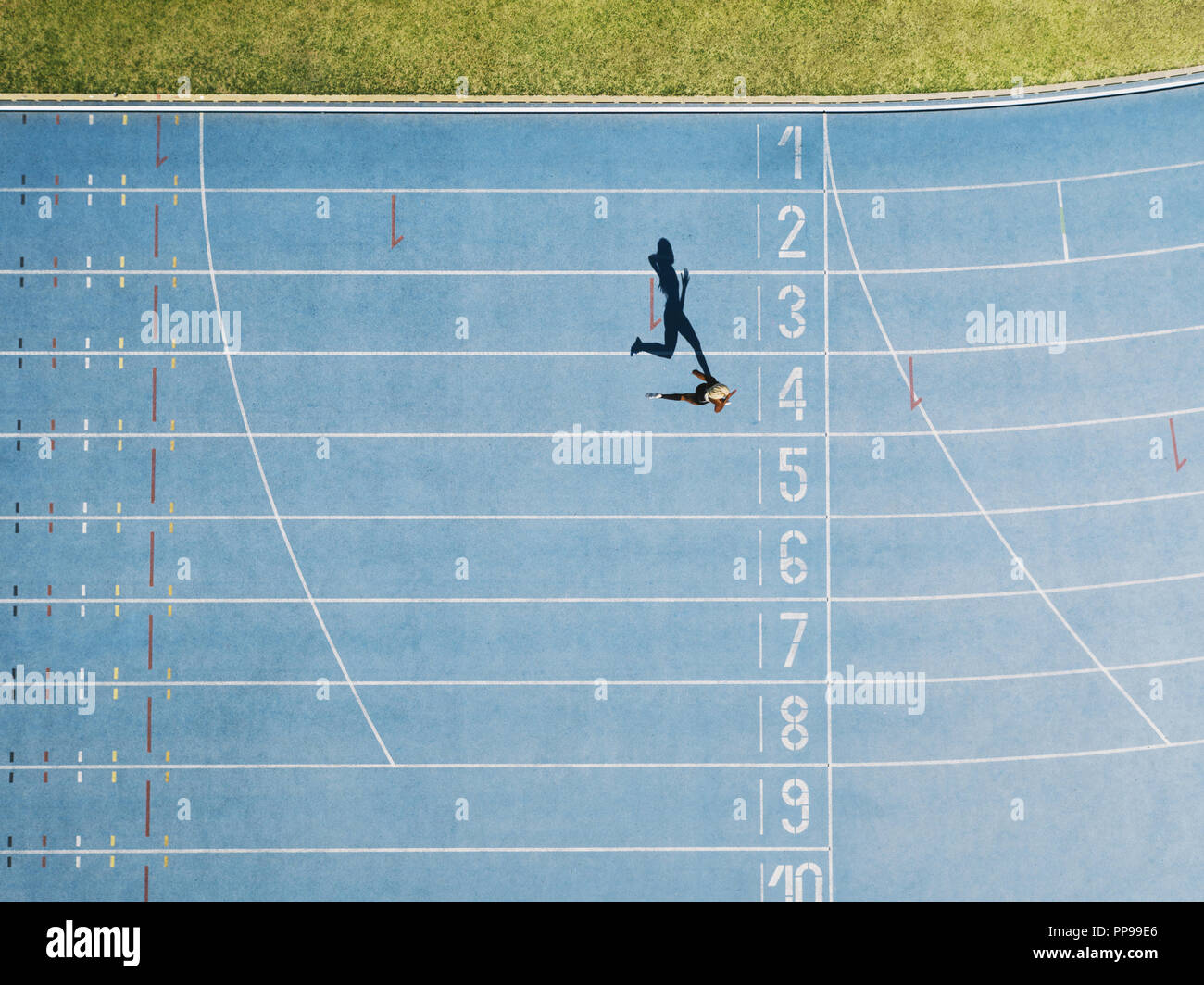 Female sprinter running on athletic track nearing the finish line. Top view of a sprinter running on race track in a stadium. Stock Photo