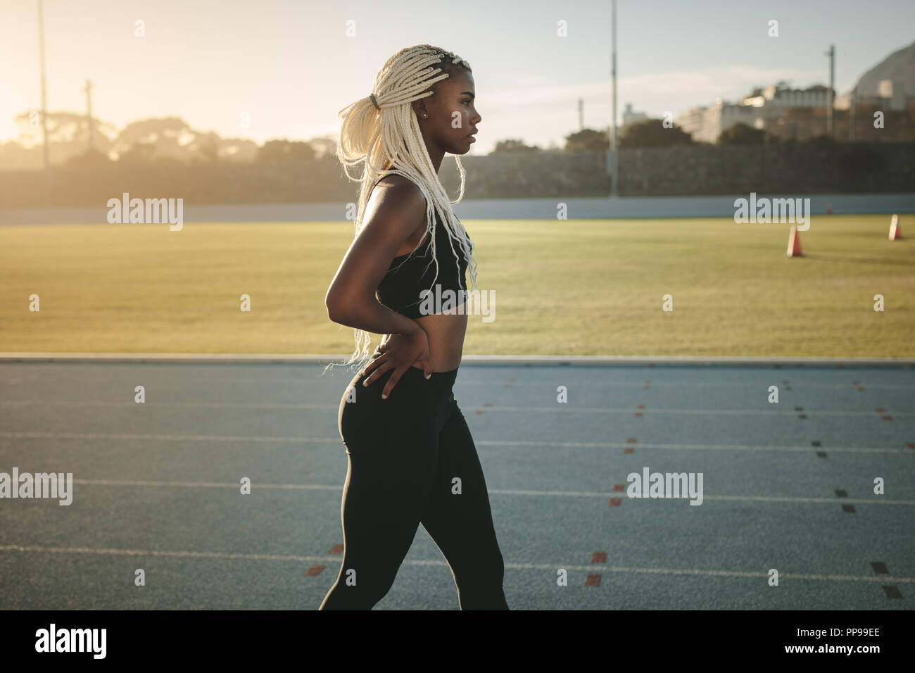 Tall athletic woman running away on the new track outdoors next to a  walkway. On a