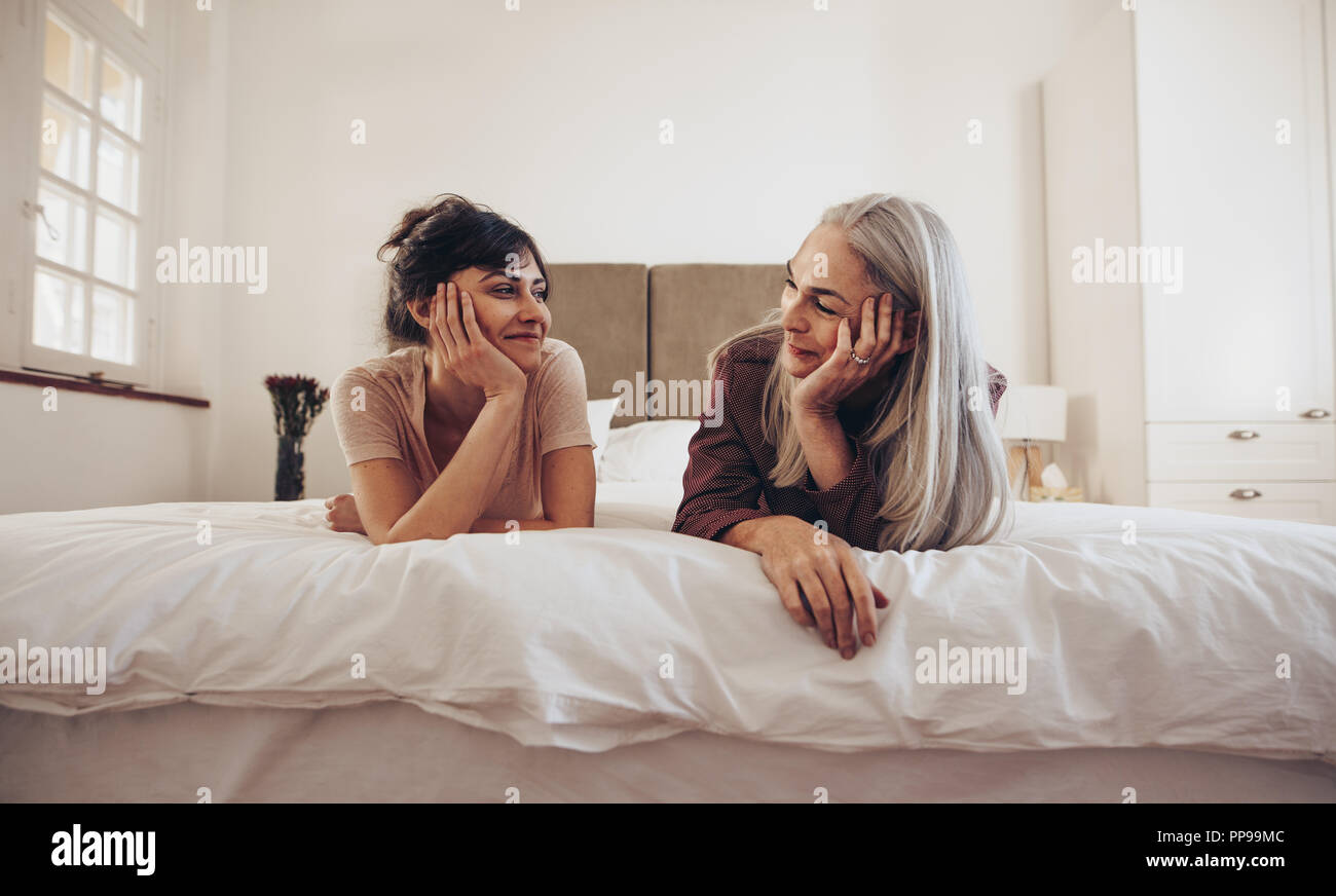 Mother and daughter on bed looking at each other lying on bed with their heads resting on palms. Woman talking to her elderly mother lying on bed at h Stock Photo