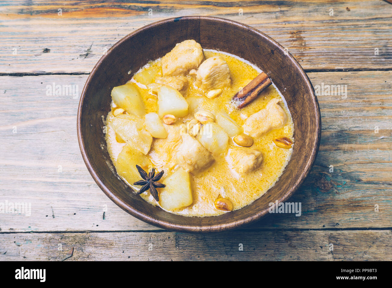 Thai massaman curry (chicken curry) with cinnamon sticks and plane riсe on wooden background. Coconut milk curry. Stock Photo