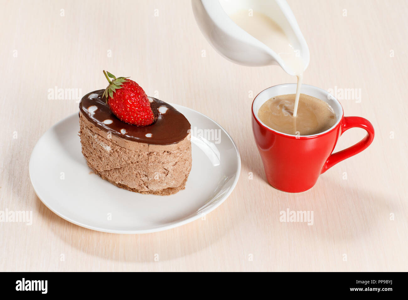Chocolate cake with strawberry on the white plate, a cup of coffee in which milk is added from a gravy boat Stock Photo