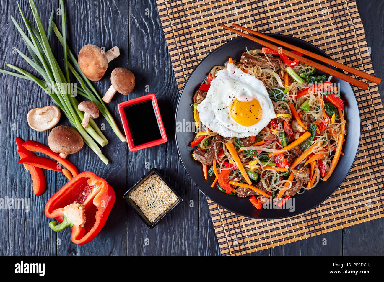 Japchae glass noodles with vegetables: spinach, red bell pepper, onion, carrot, garlic, shiitake mushrooms and beef, dressed with mix of sesame seeds  Stock Photo