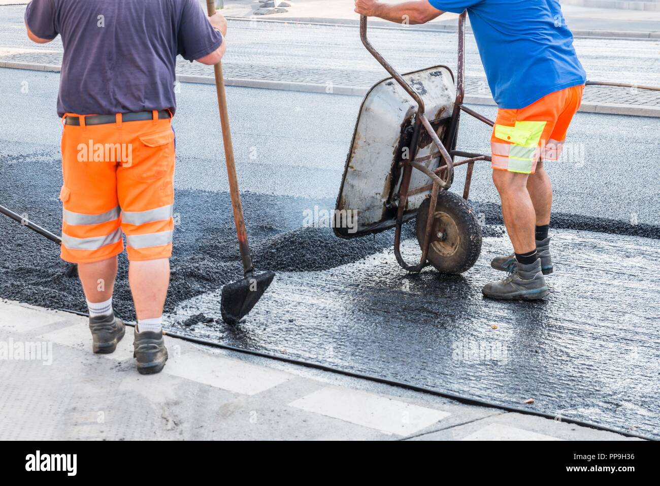 Road workers distribute the hot asphalt on the road with shovels and ...