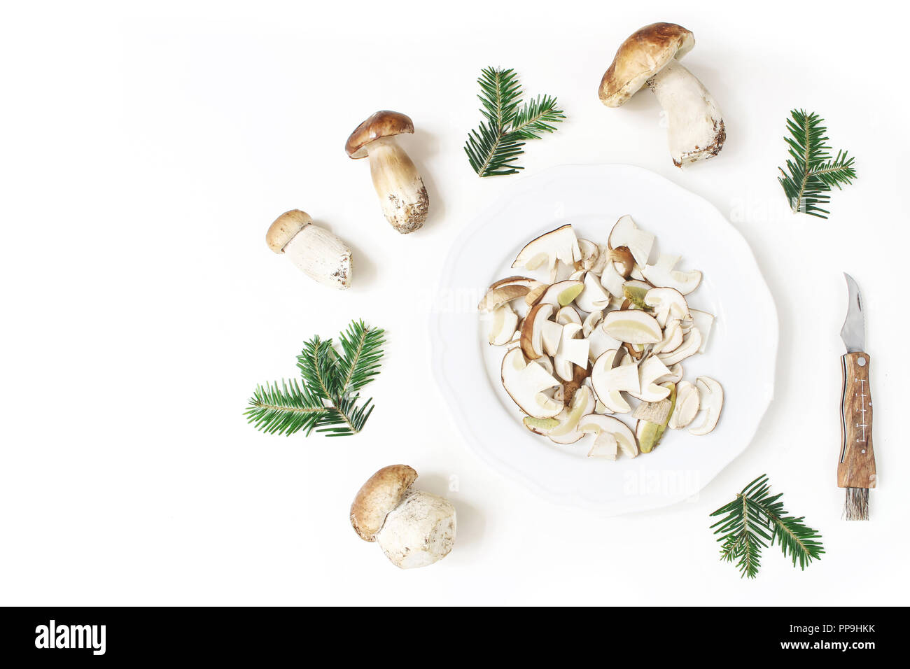 Autumn styled food arrangement. Composition of whole and sliced porcino mushrooms, Boletus edulis on white plate, fir branches and pocket knife. White table background. Fall design, flat lay, top view Stock Photo