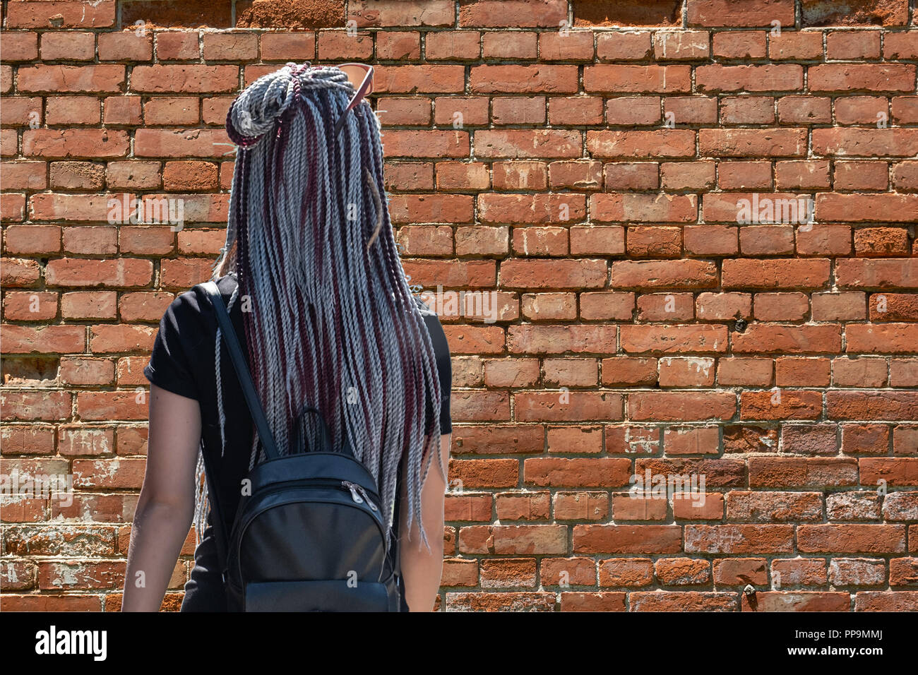 A girl with hair braided in braids stands with her back and looks 