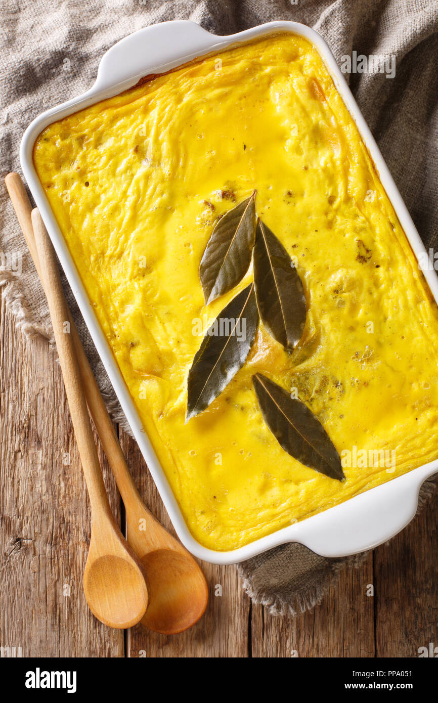 Delicious hot South African food Bobotie spicy minced meat with whipped eggs close-up in a baking dish on the table. Vertical top view from above Stock Photo