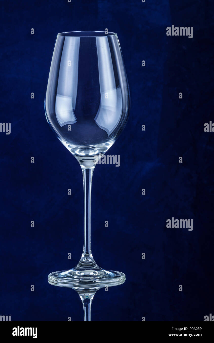 Elegant empty wine glass against a blue background on a reflective surface Stock Photo