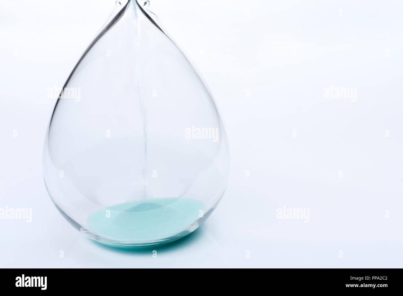 Hourglass on white background. Sand falls inside an azure-colored flask. Stock Photo