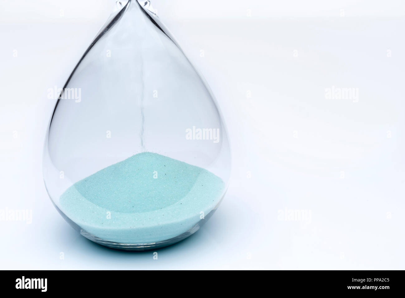 Hourglass on white background. Sand falls inside an azure-colored flask. Stock Photo