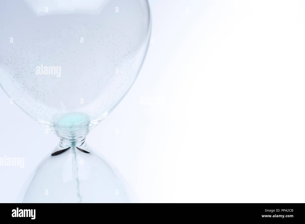 Hourglass on white background. Sand falls inside an azure-colored flask. Stock Photo
