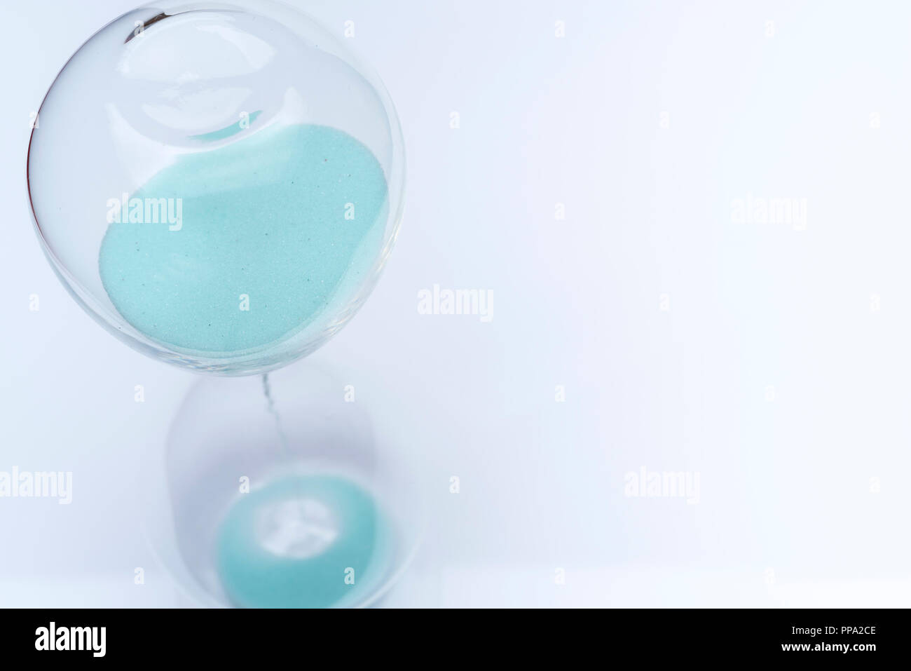 Hourglass on white background. Sand falls inside an azure-colored flask. Stock Photo