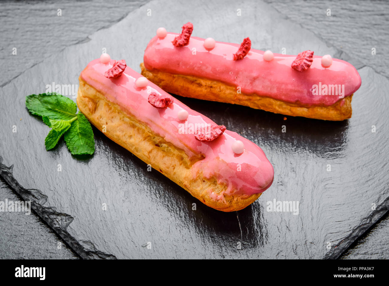 Traditional French dessert. Eclair with chocolate icing and raspberries. Stock Photo