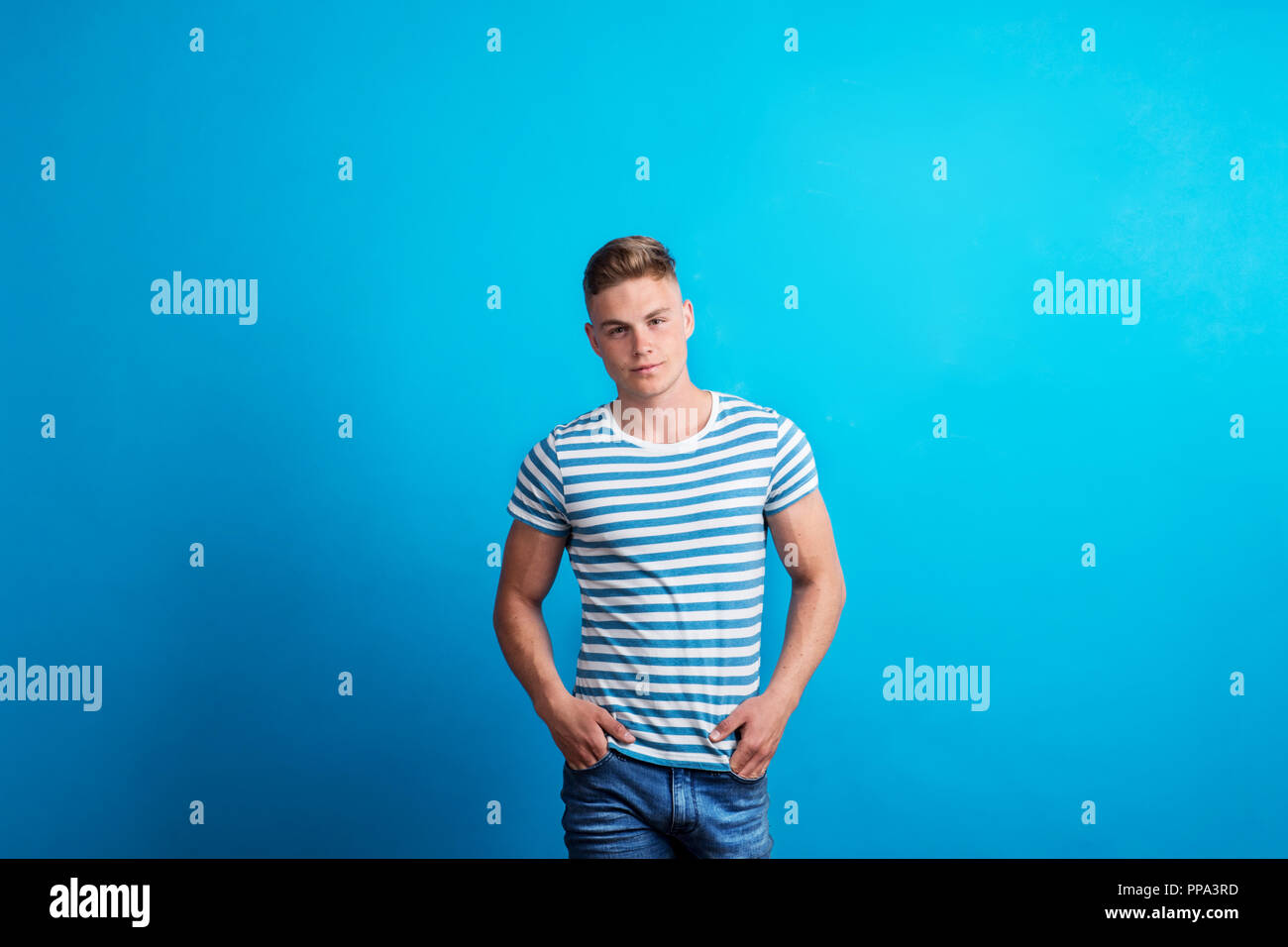 Portrait of a young man in a studio standing against blue background ...