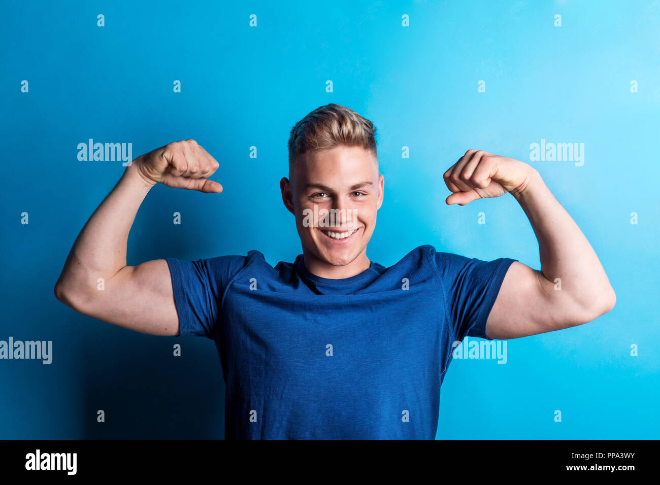 Portrait of a cheerful young man in a studio, flexing muscles. Stock Photo