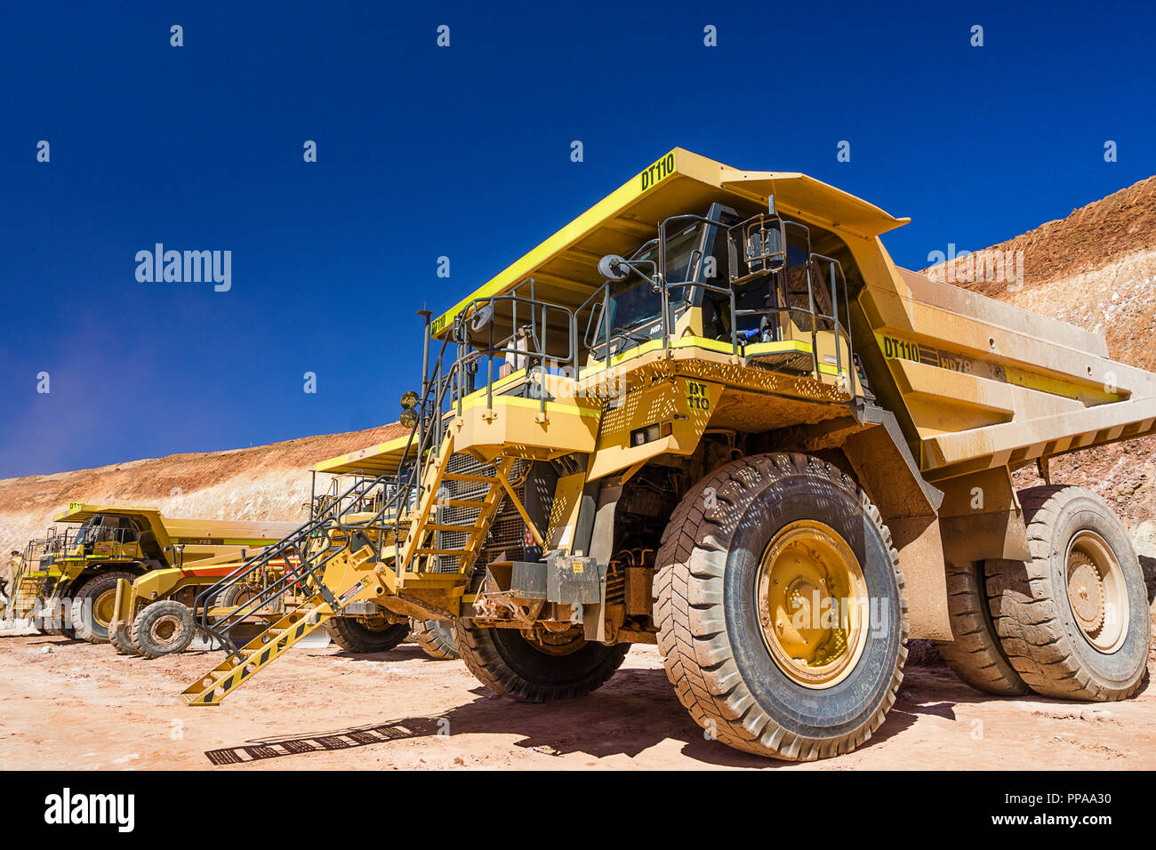 Large yellow dump trucks parked up on floor of open pit mine, Western Australia Stock Photo