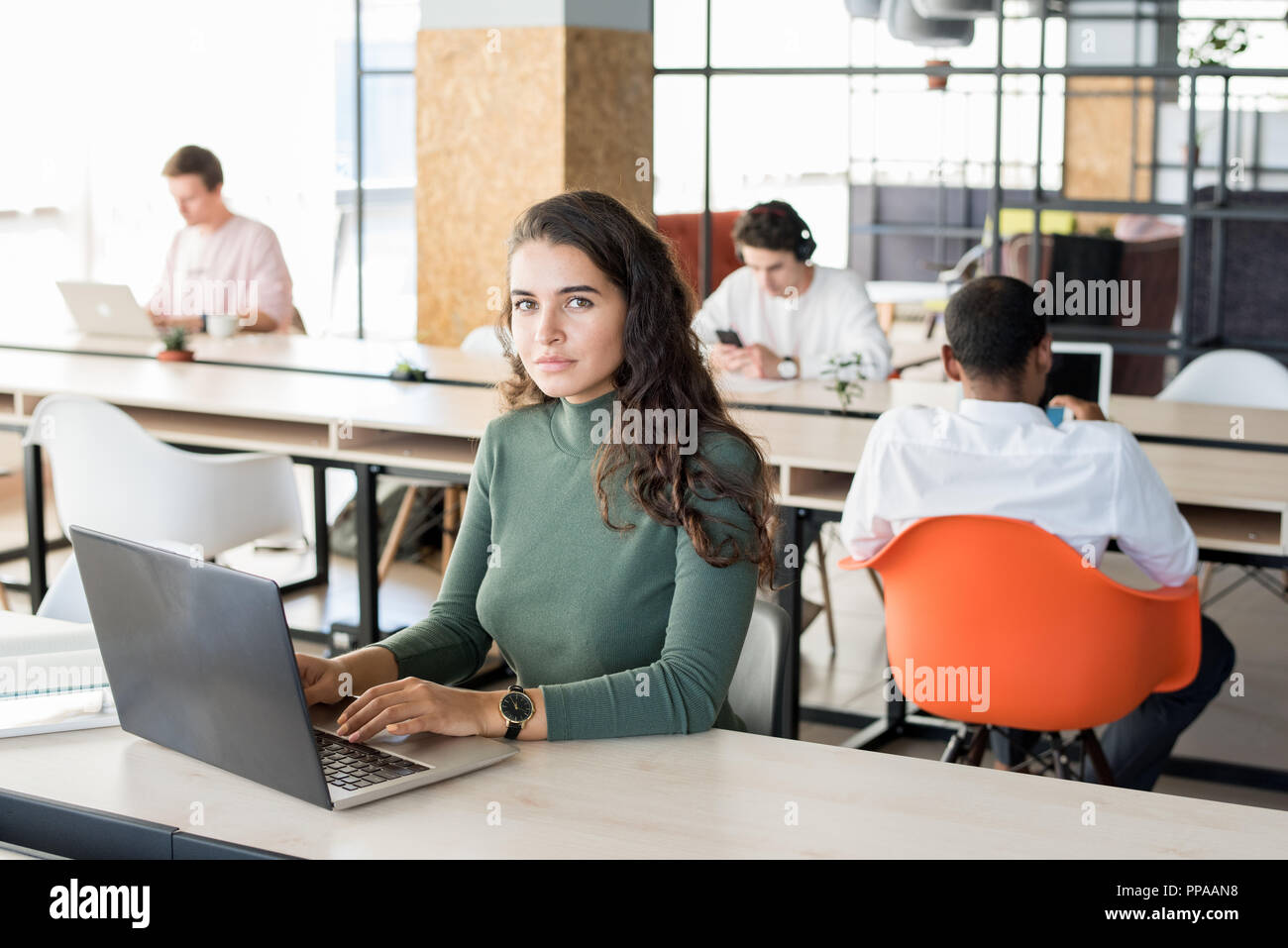 Portrait of beautiful young woman looking at camera while working with laptop in modem open office, copy space Stock Photo