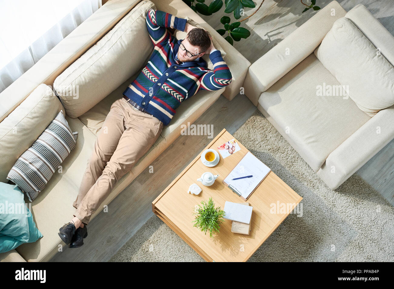 Above view portrait of pensive male psychologist relaxing after session while lying on  couch in sunlit office, copy space Stock Photo