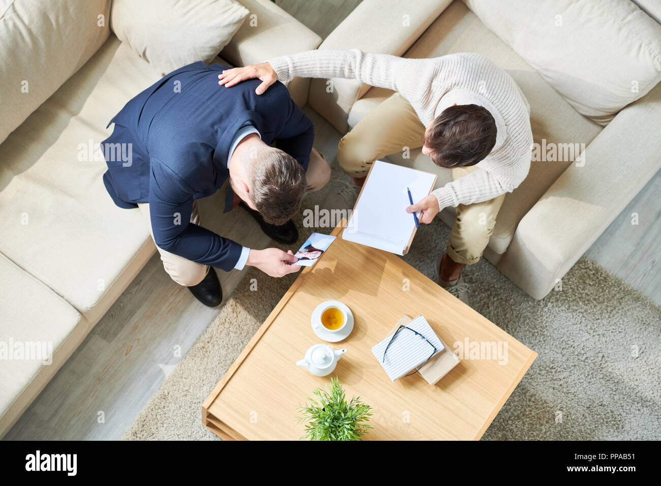Above view portrait of psychiatrist consulting grieving young man holding photo of wife, copy space Stock Photo