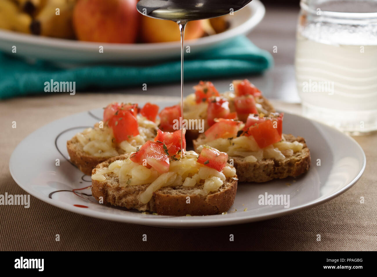 Close-up of spoon pouring olive oil in a bruschetta with mozzarella, tomatoes and oregano; selective focus. Stock Photo