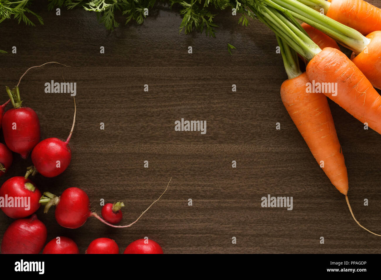Salad ingredients on a flat dark brown wooden board. Carrots and radishes, top view, with copy space for text. Stock Photo
