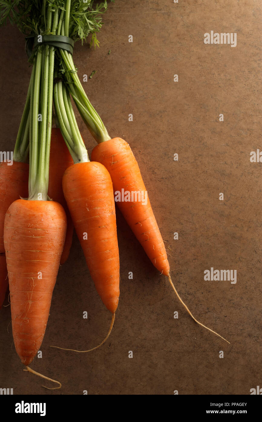 Fresh carrots on a flat wooden board under morning light; top view, with copy space for text; healthy food concept. Stock Photo