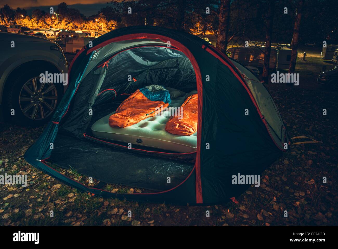 Inside Illuminated Tent on the Campsite at Night. Two Sleeping Bags Inside. Traveling with Tent Theme. Stock Photo