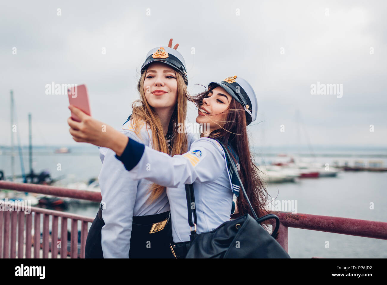 Two college women students of Marine academy taking selfie by sea wearing uniform. Happy friends having fun on pier Stock Photo
