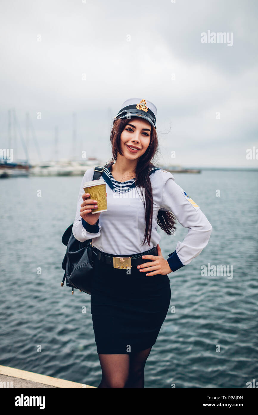 College woman student of Marine academy drinking coffee by sea wearing uniform. Girl walking in seaport of Odessa on pier Stock Photo